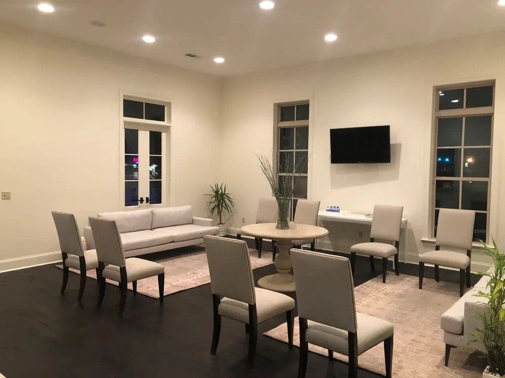 Modern dining room with beige chairs and a TV on the wall.